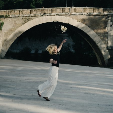 Ingeborg Bachmann (Sandra Hüller) hört Musik und tanzt unbeschwingt dazu am Ufer des Tibers in Rom.